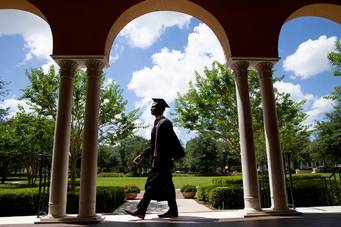 A student wearing a cap and gown walking on campus.