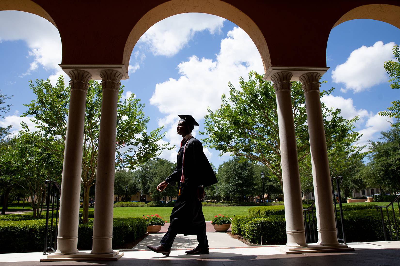 A student in a cap and gown walking across Rollins campus