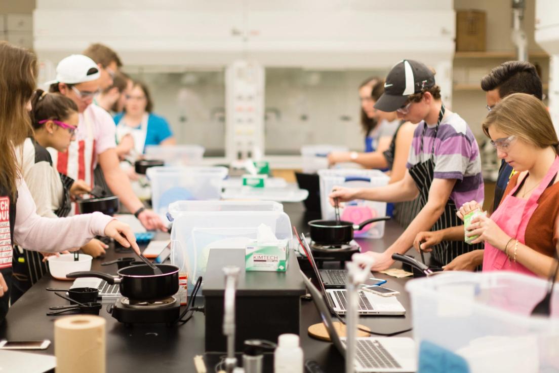 A group of students gathered around a large table during a chemistry experiment.