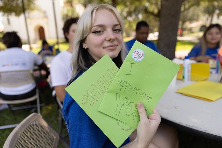 A student holds two handmade cards up to the camera.
