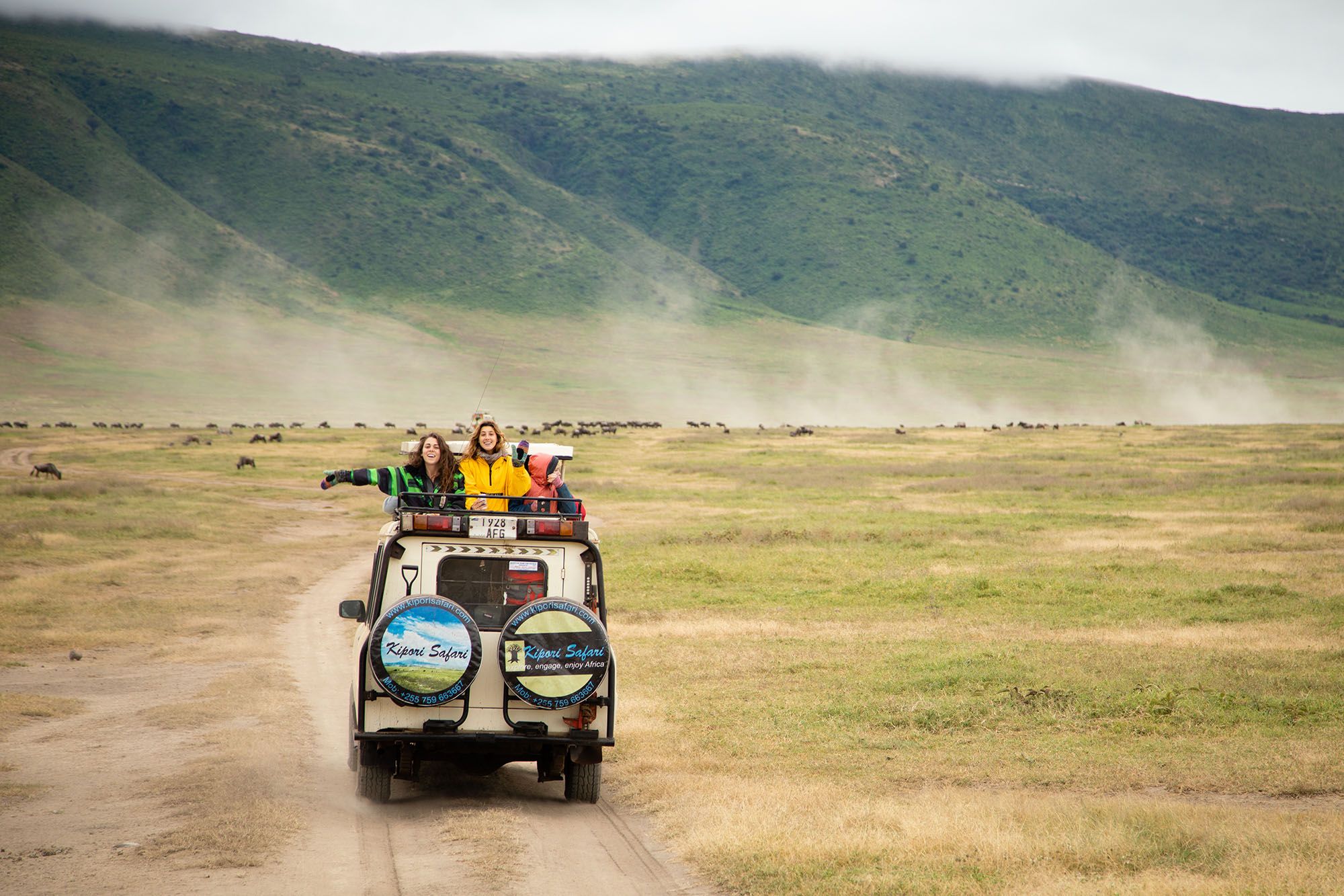 Two students wave at the camera from the back of a safari jeep in Tanzania.