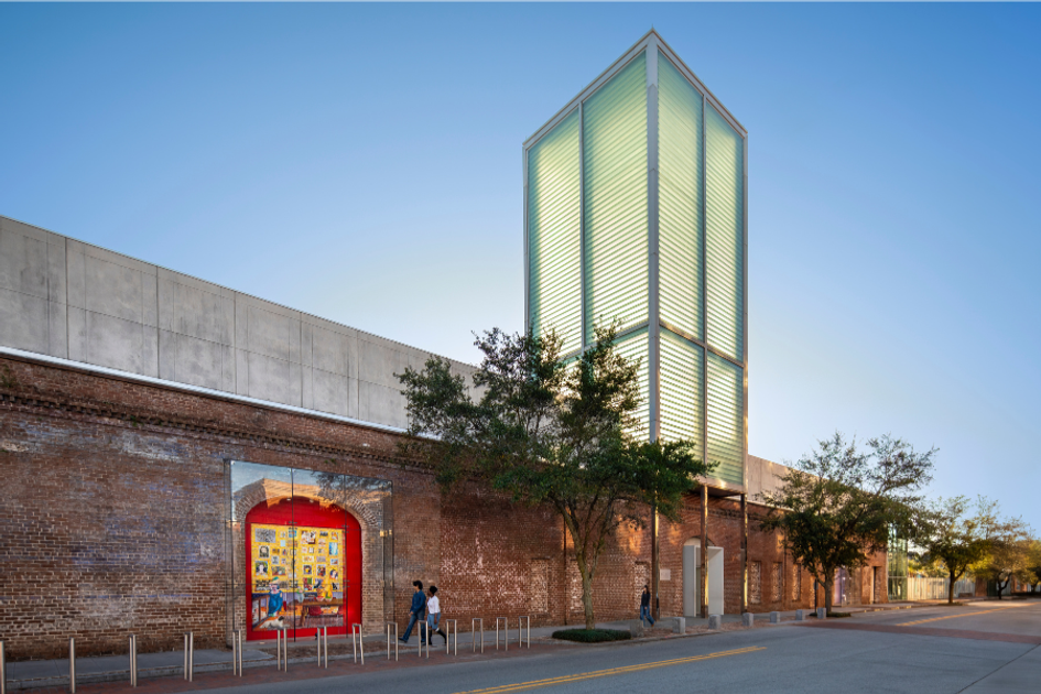 Contemporary museum exterior with glowing glass tower and brick facade at dusk