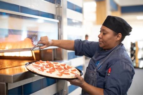 Chef putting a pepperoni pizza into an oven.