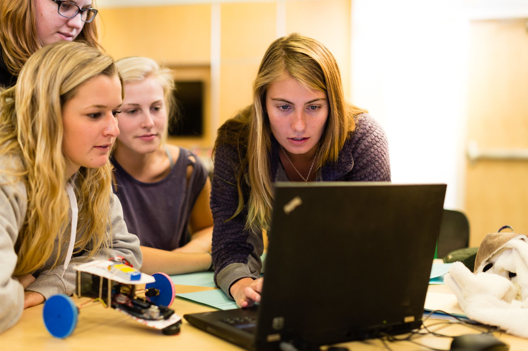 Three students gathered around a laptop working on a project in Computer Science.