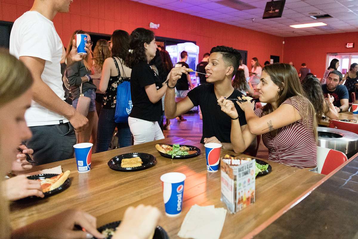 Two students eat pizza in a bowling alley.