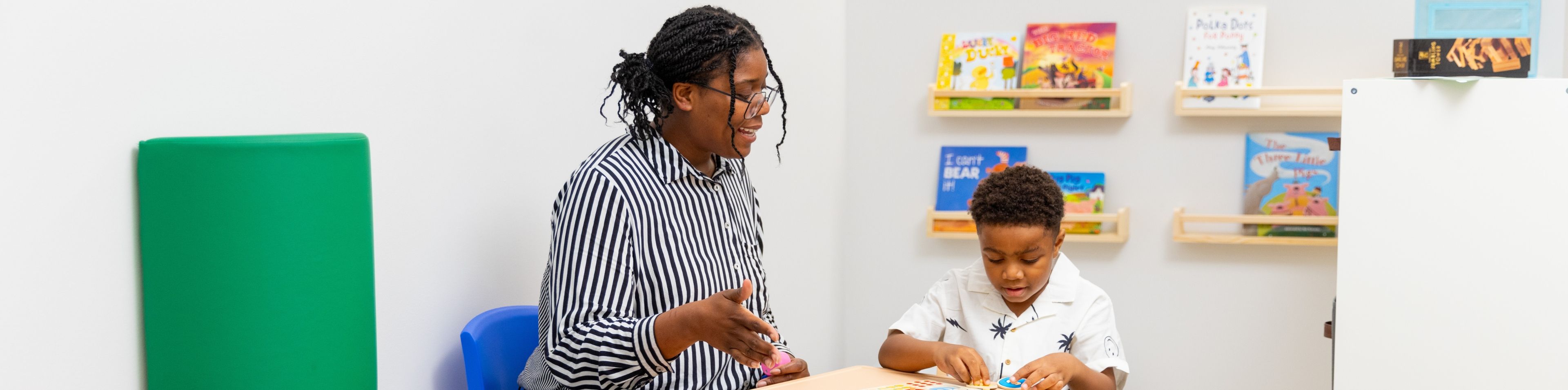 A behavior analyst helps a young patient assemble a colorful foam puzzle.