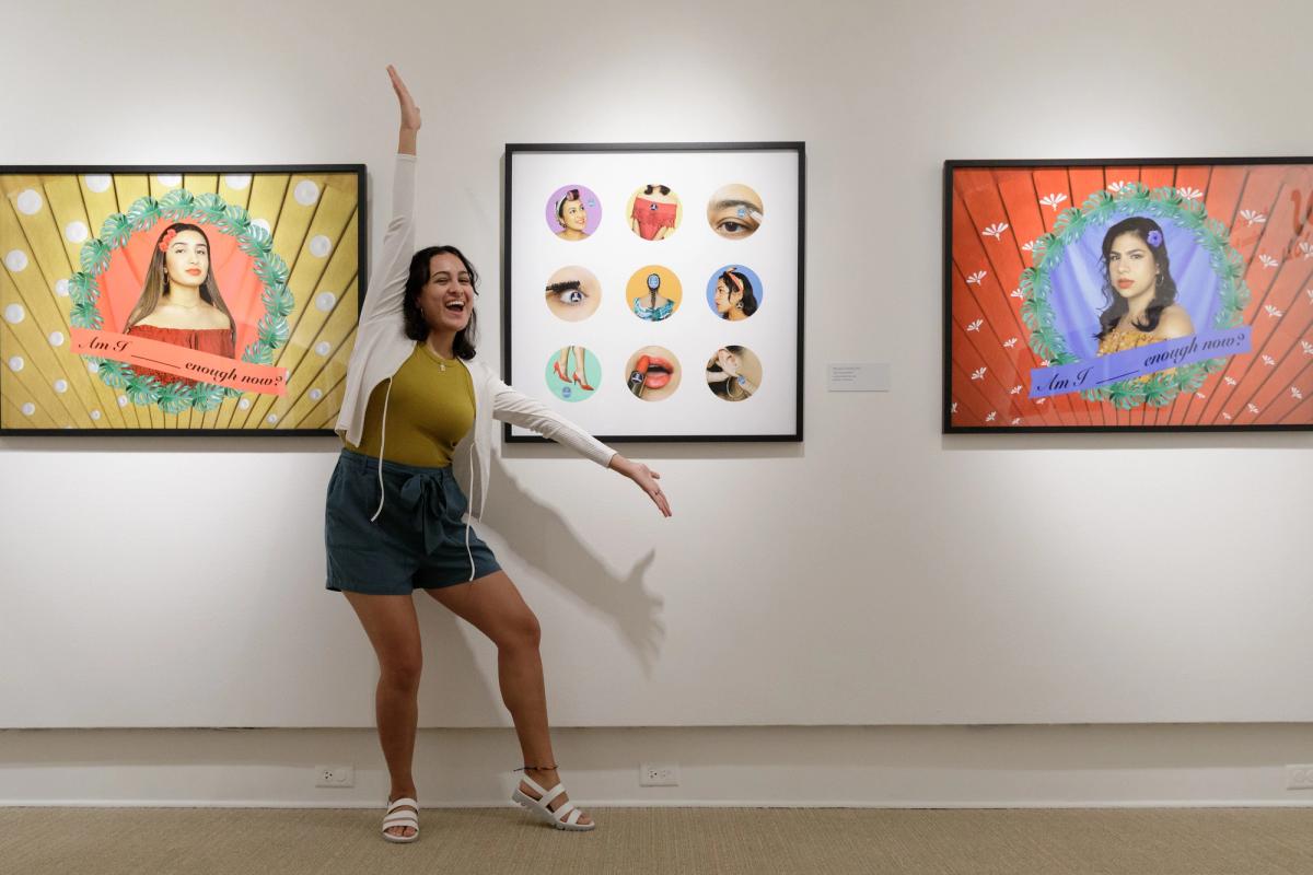 Student with arms extended showcasing three framed pieces of art on museum wall.