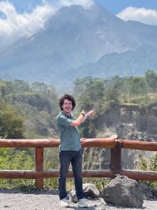 Smiling traveler points toward towering volcano from scenic overlook.