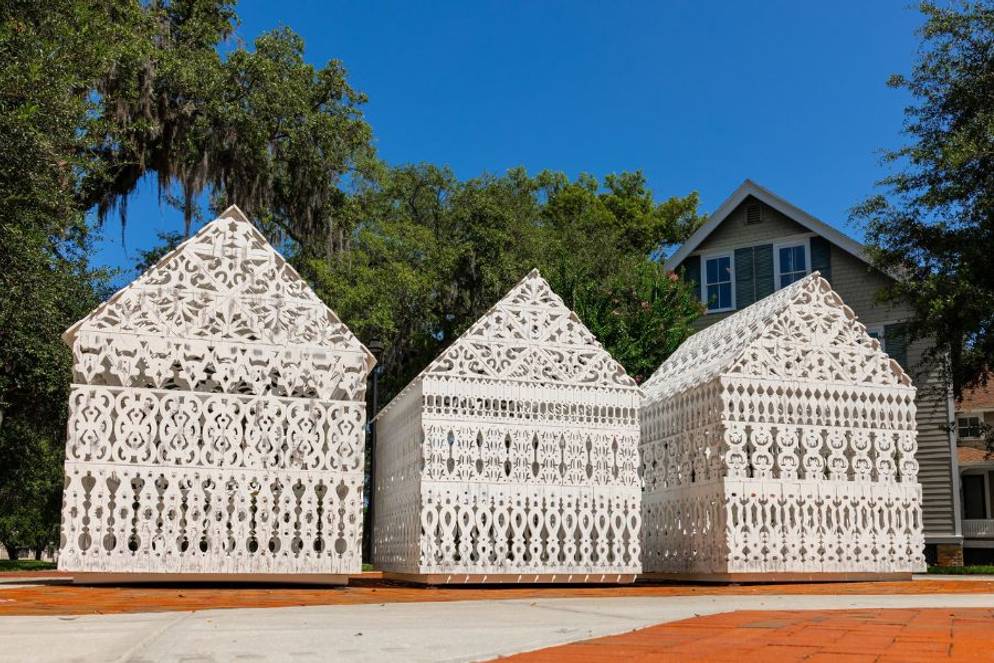 Three house-shaped sculptures feature intricate white lattice patterns outdoors.