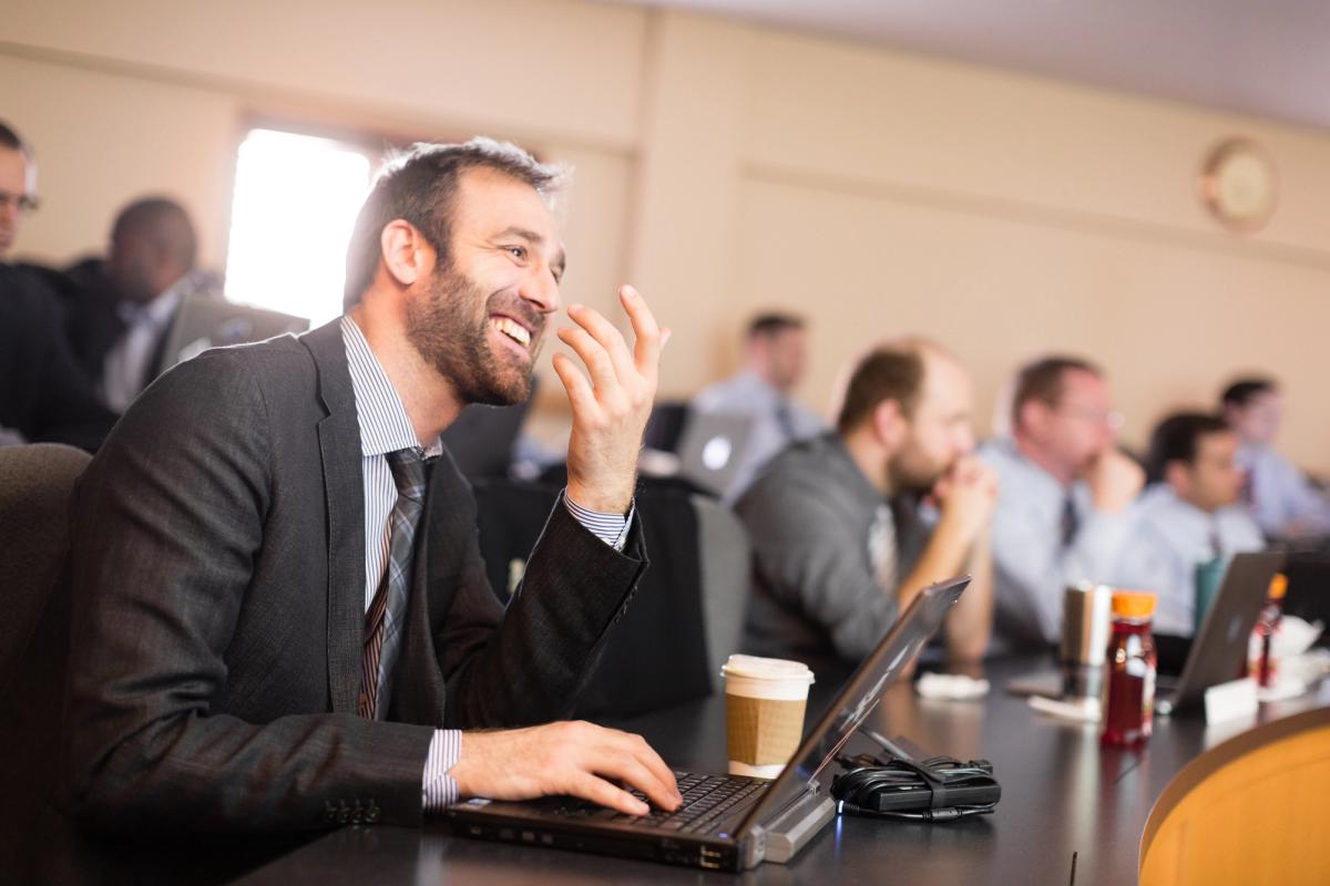 Man in business suit in classroom, with laptop and coffee cup.