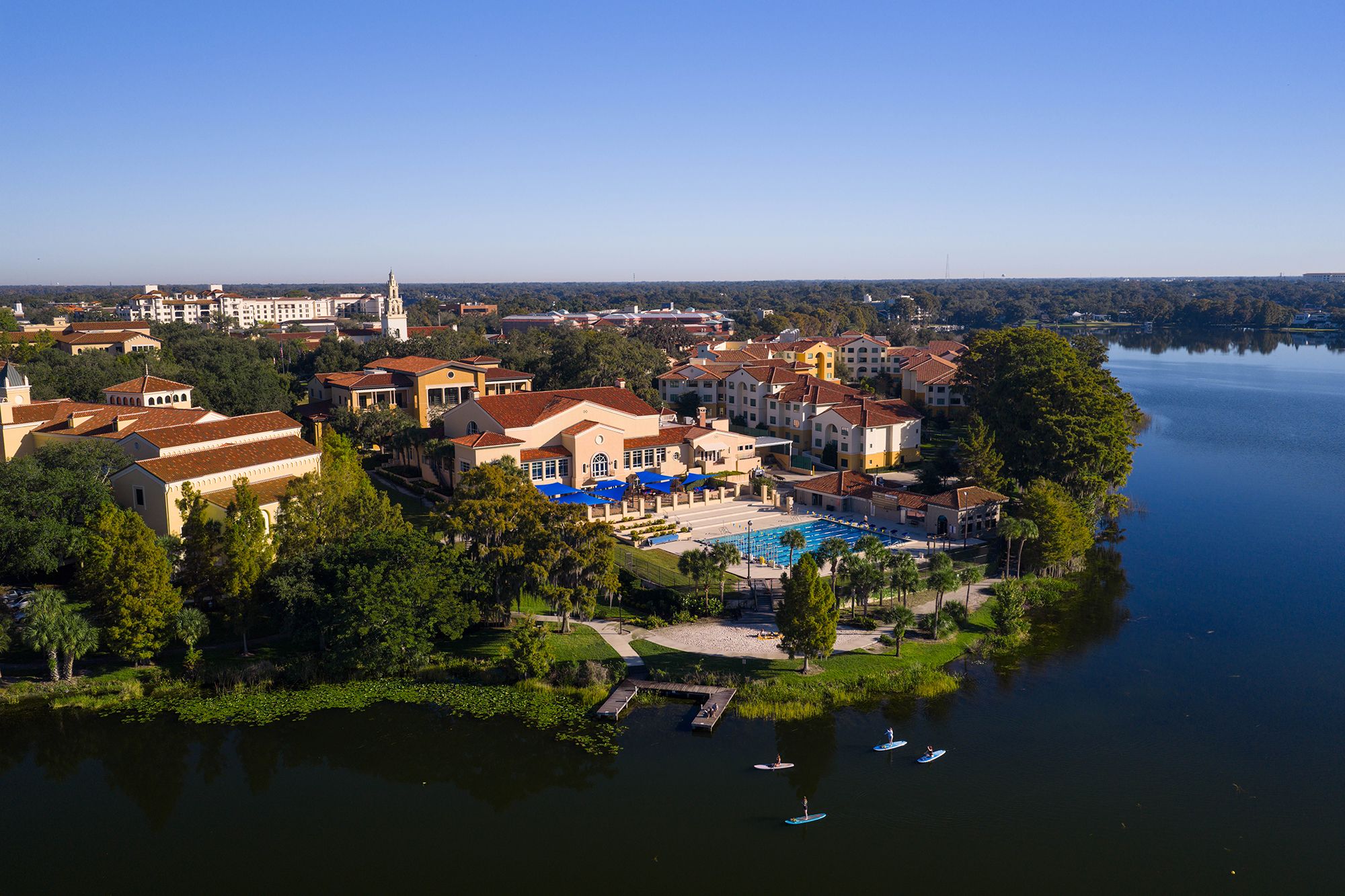 Lakeside campus with pool, red-roofed buildings, and paddleboarders on water