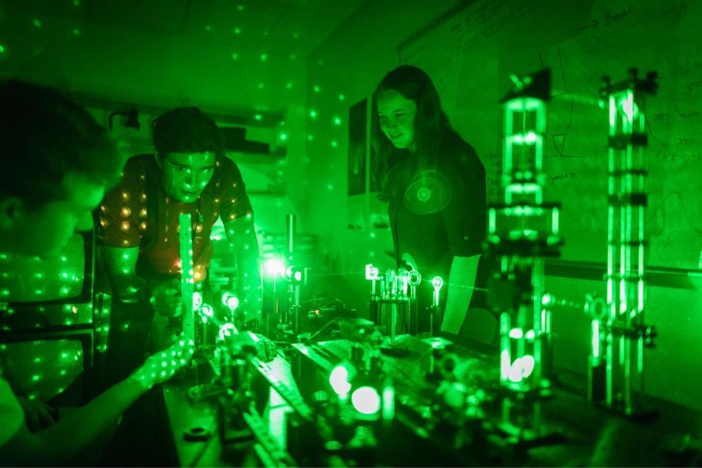 A professor and two students conduct physics research.