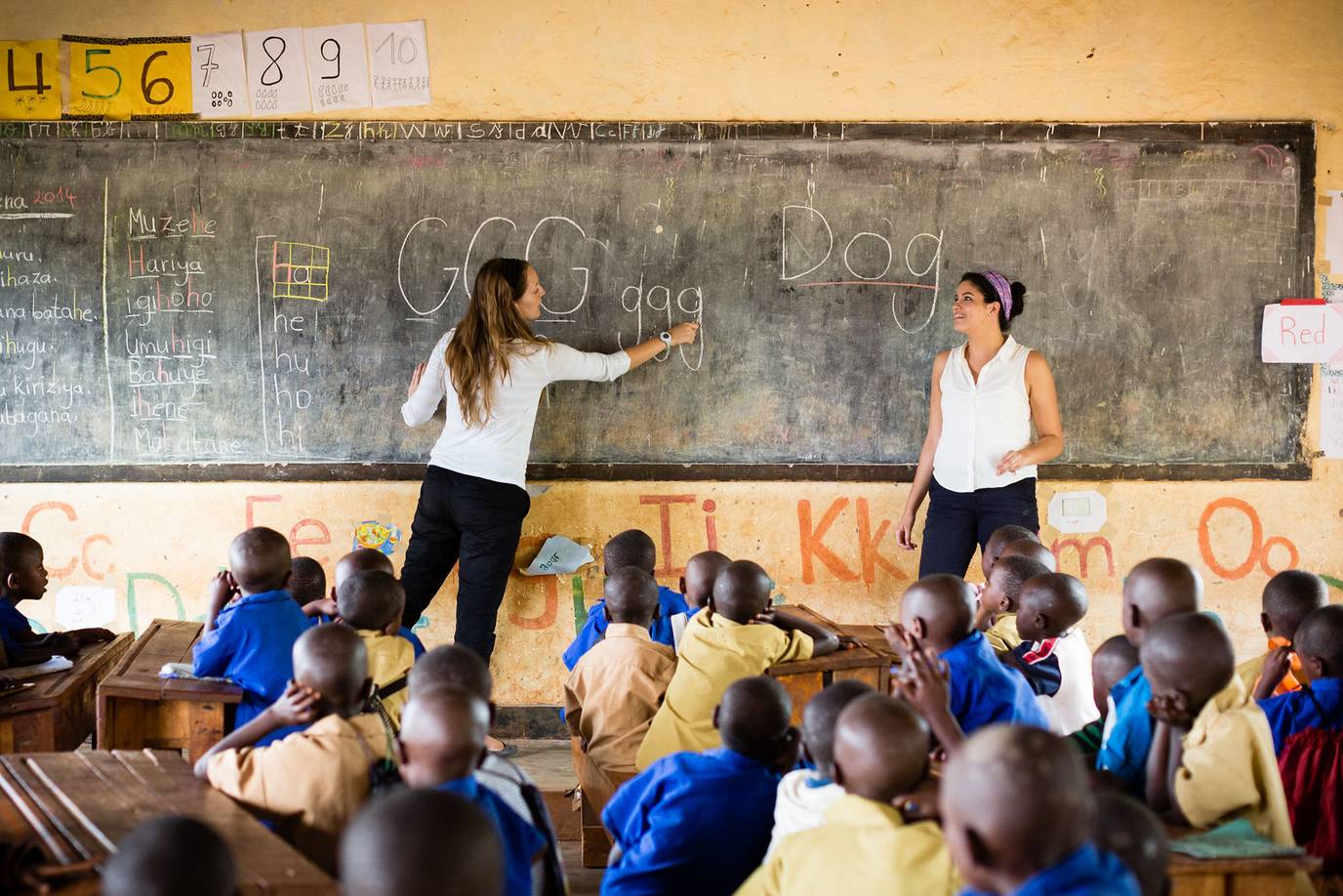 Rollins students draw English words and letters on a chalkboard in a Rwandan classroom.