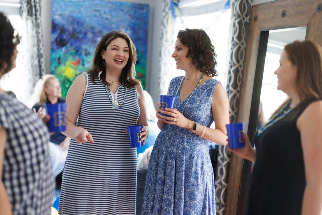 Four women stand in a semi-circle chatting during an alumni event.