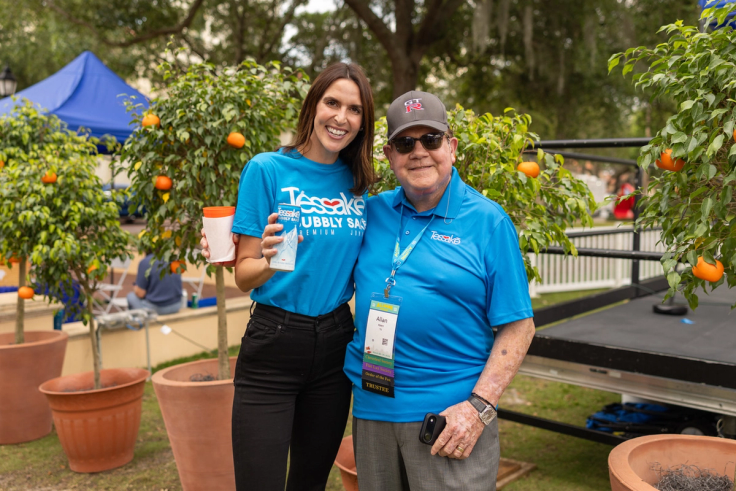 Alumni Tessa Hahn ’10 and Allan E. Keen '70 '71MBA '10H pictured in front of orange trees and a stage at the Grove Party.