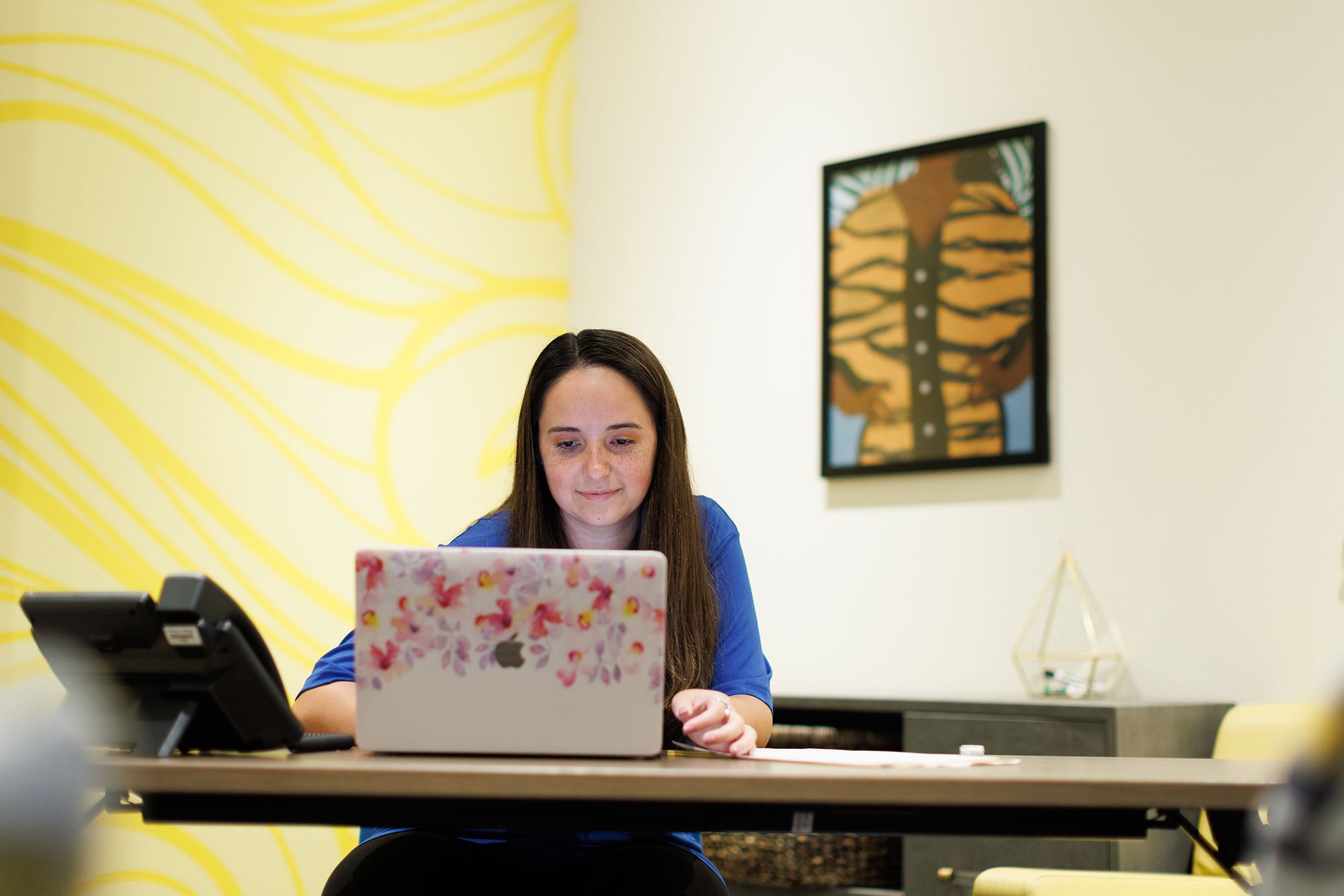 A graduate assistant works on her laptop in an office on campus.