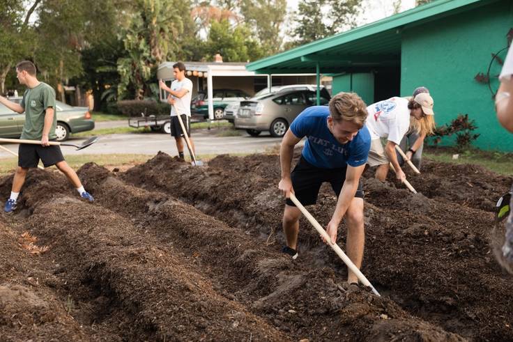 Students digging in the soil to turn a residential lawn into a micro farm.