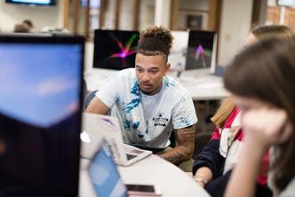 Critical media professor interacts with two students in class.