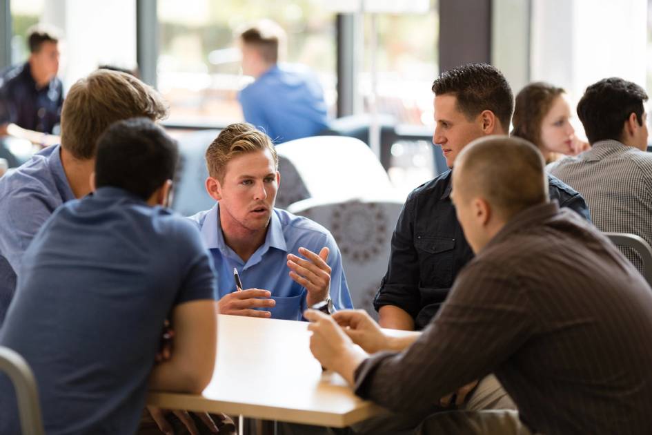 A group of young adults conversing at tables in a common area.