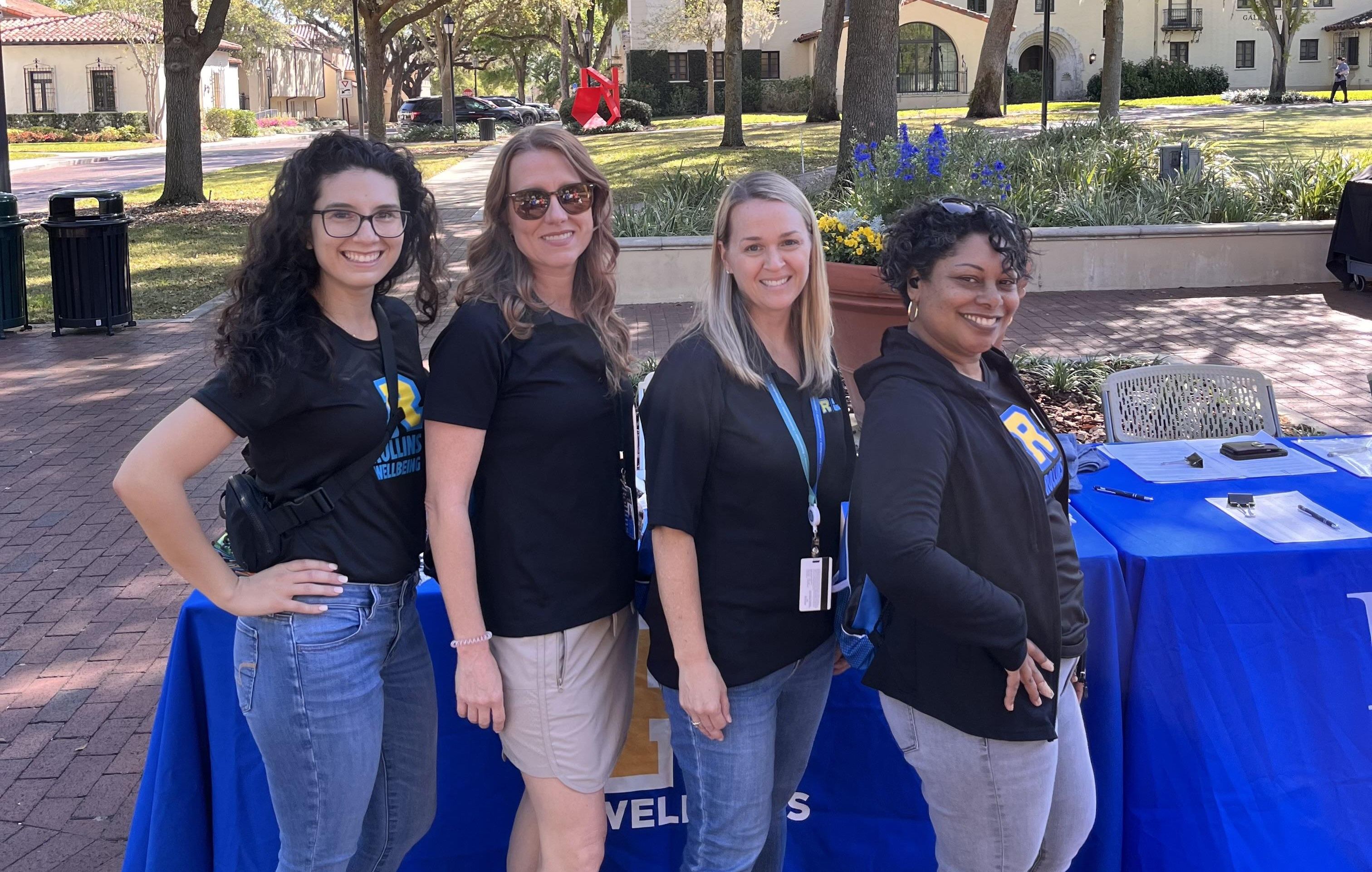 4 Rollins employees posing in front of table.