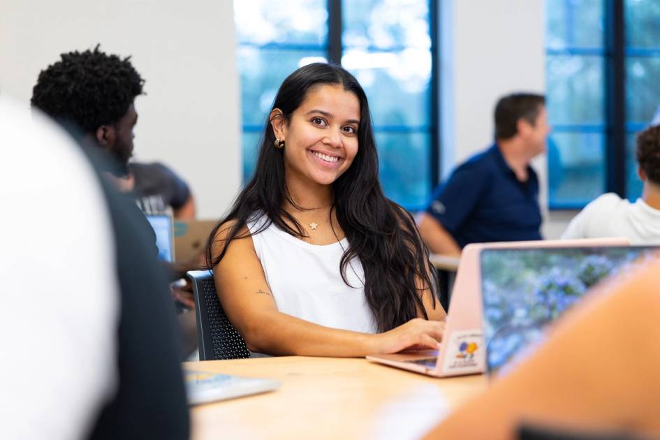 A student in a Rollins Professional Advancement classroom smiles at the camera.
