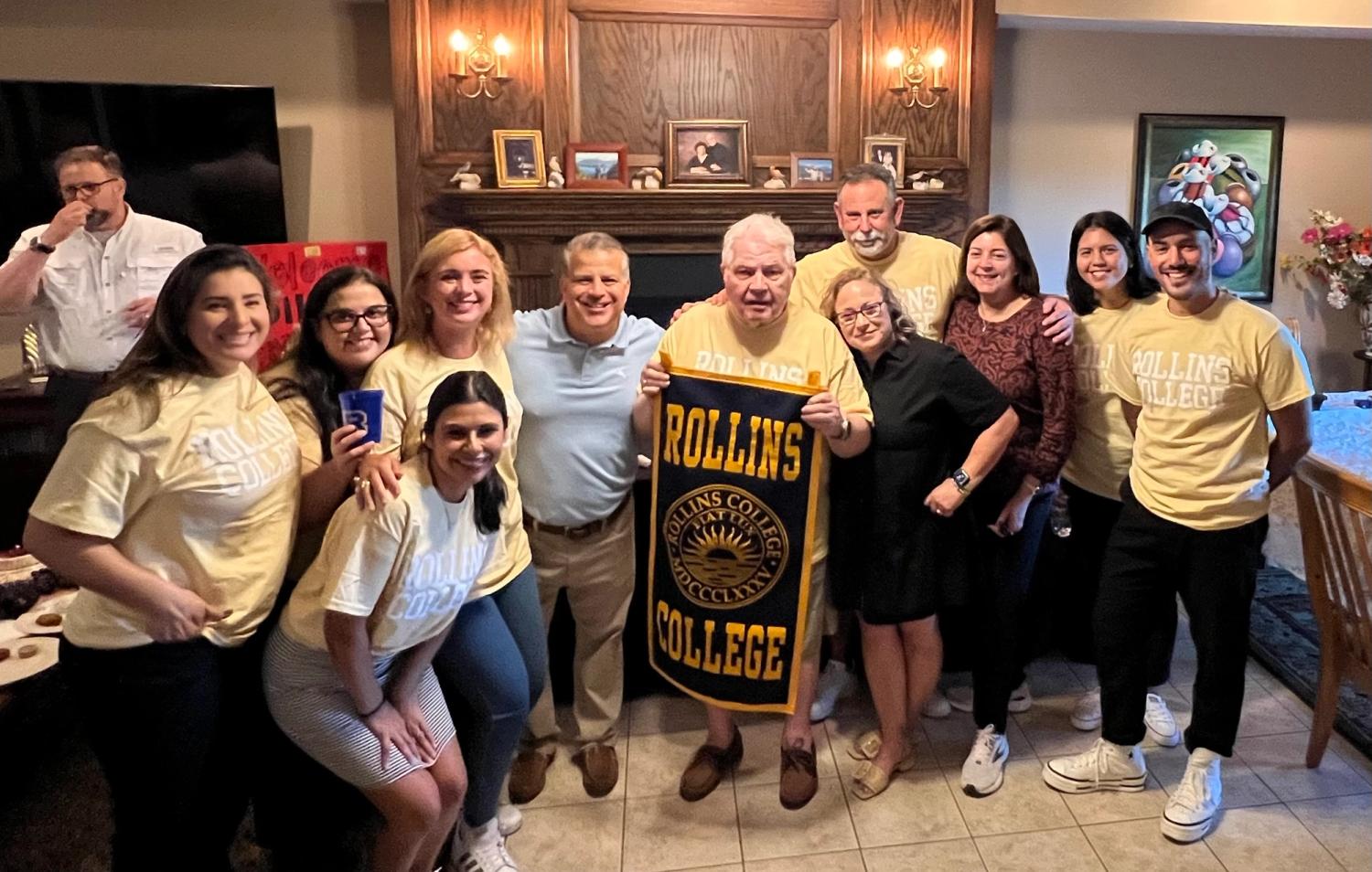 Rollins alumni celebration with faculty member, holding Rollins College banner