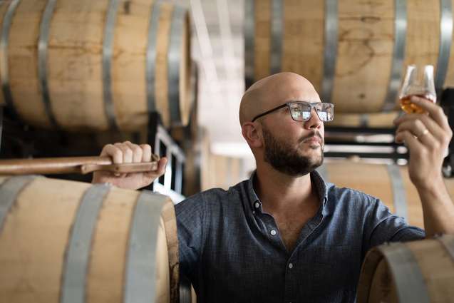 A Rollins alumn holding up a glass of whiskey in his distillery.