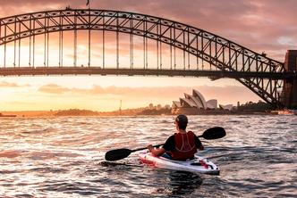 Student kayaking near the Sydney Australia bridge and opera house at sunset.