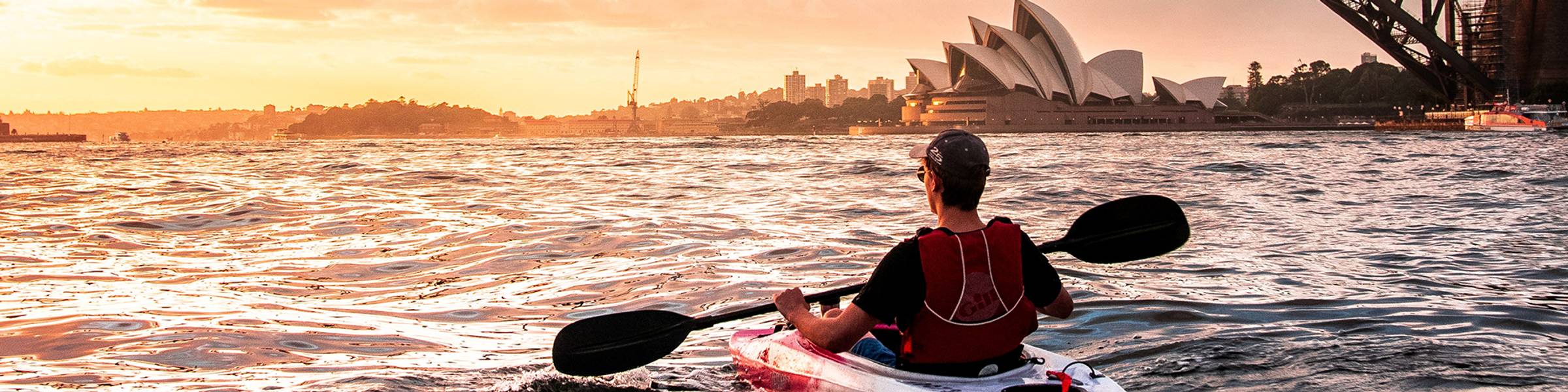 Student kayaking near the Sydney Australia bridge and opera house at sunset.