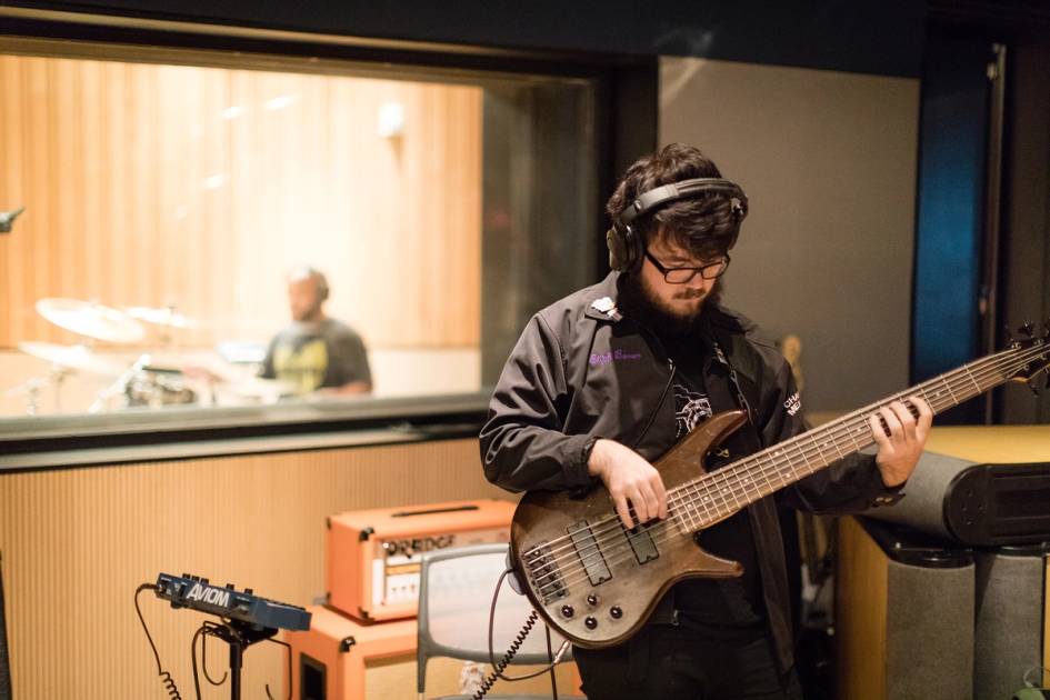 Rollins student plays guitar in recording studio with drummer in background