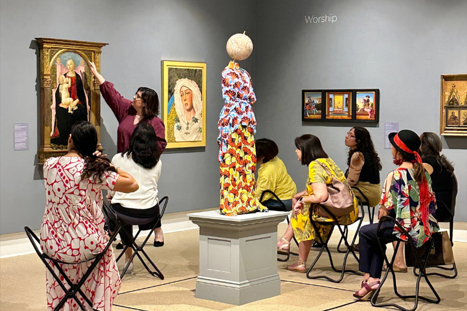 Woman points to artwork surrounded by people seated in an art gallery