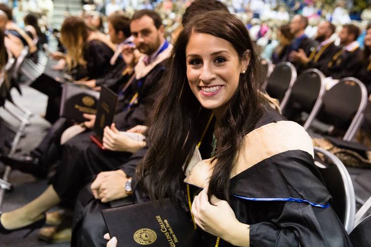 Female in graduate hood, cap, and gown at graduation ceremony. 