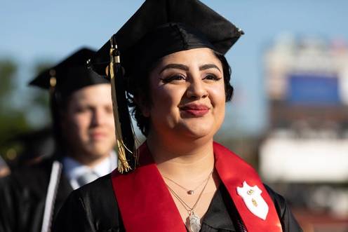 A graduate in a cap and gown smiles during a commencement ceremony.
