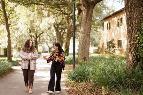 A student mentee walks and talks with her alumni mentor on Rollins’ campus.