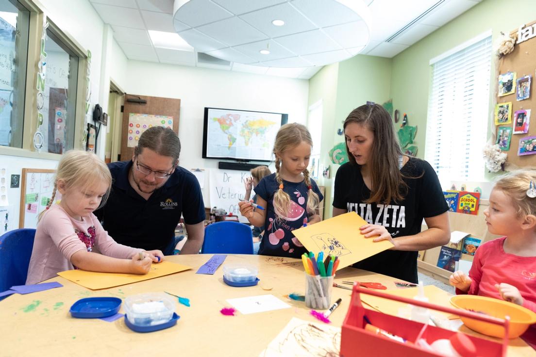 Professor Matthew Forsythe and his assistant working with three children coloring at a table in the CDC.