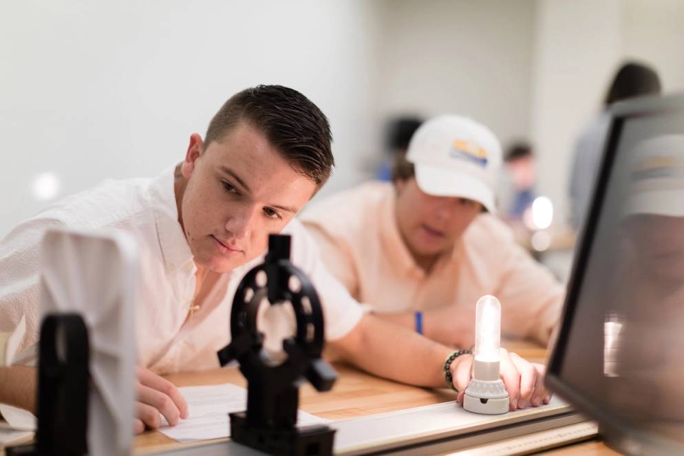 A student moving a lightbulb on a desk getting a reading from different distances.