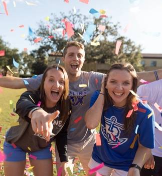 A group of 91 students laugh while confetti falls; one student points at the camera.