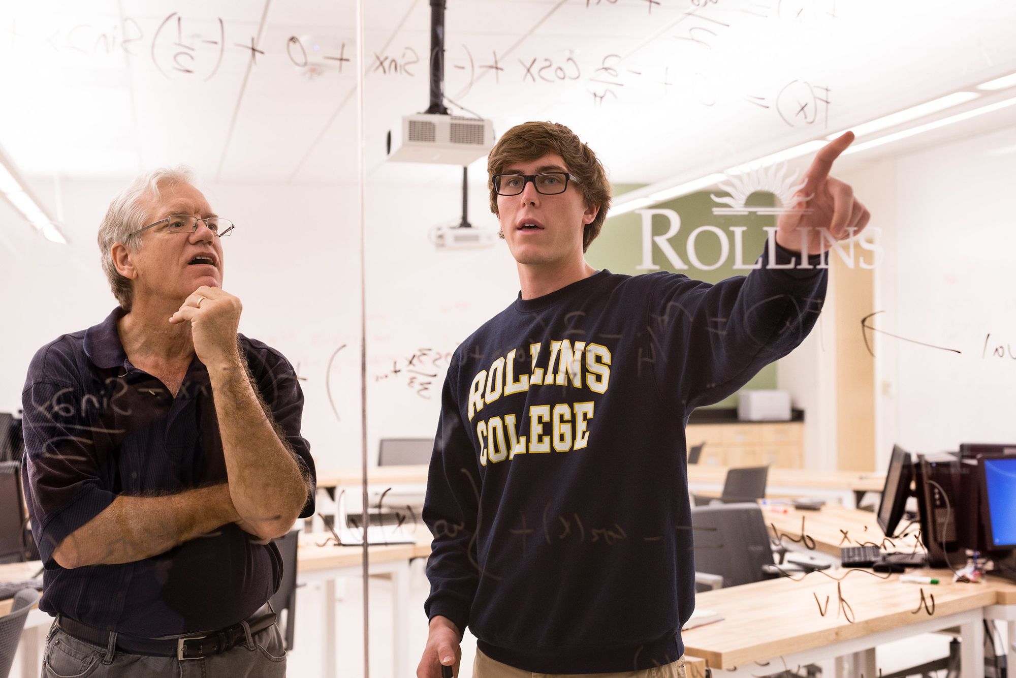 Student and professor work out math equation on glass wall.