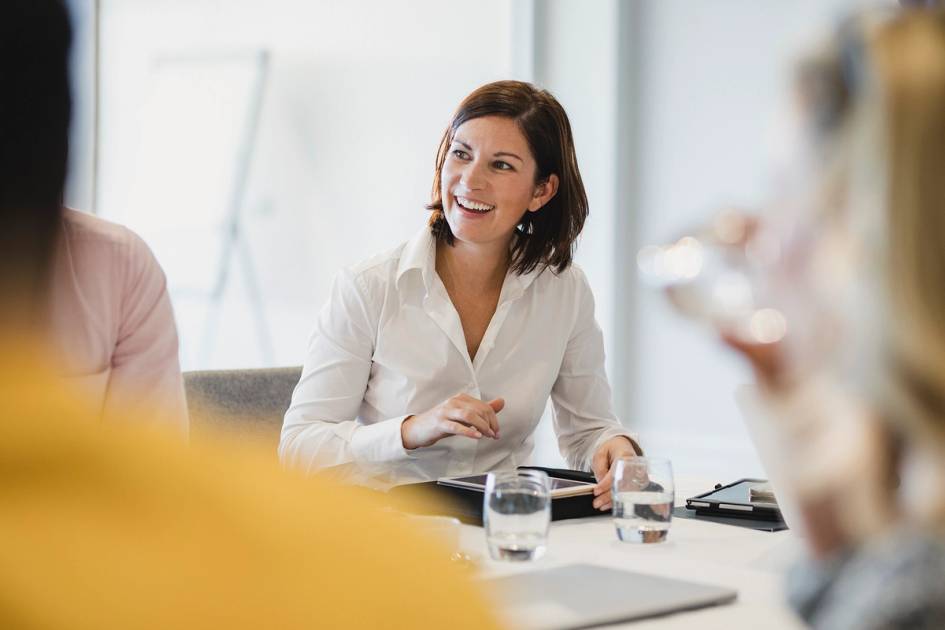 Professional smiling during a meeting, engaging with colleagues around a table