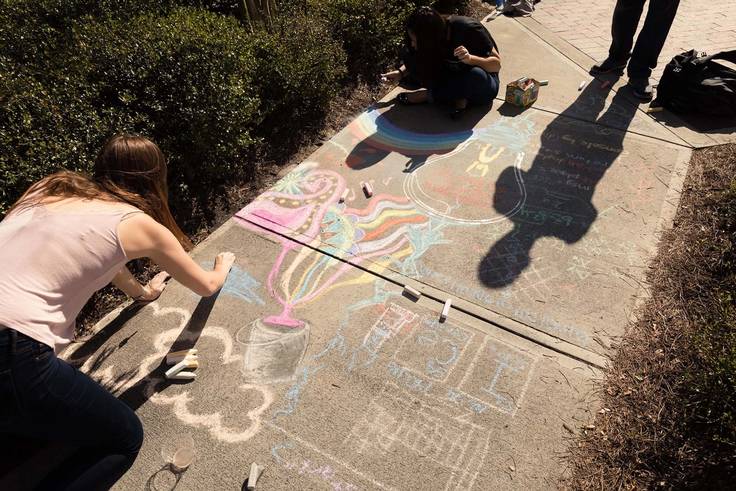 A student draws messages of kindness on a sidewalk with chalk