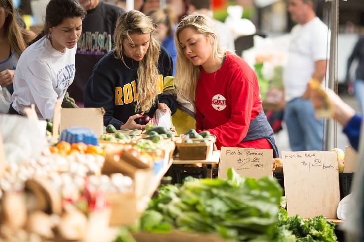 Three college students shop for produce at a farmers market