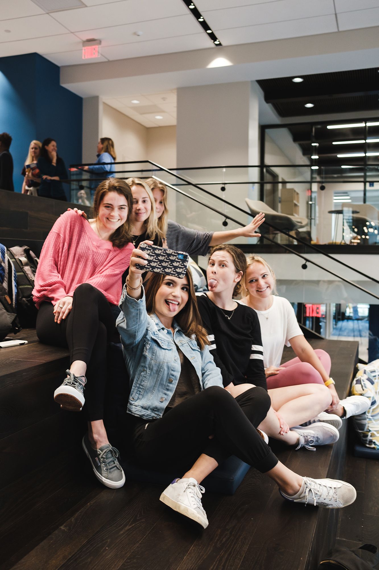 A groupf of college students taking selfies on the atrium stairs.