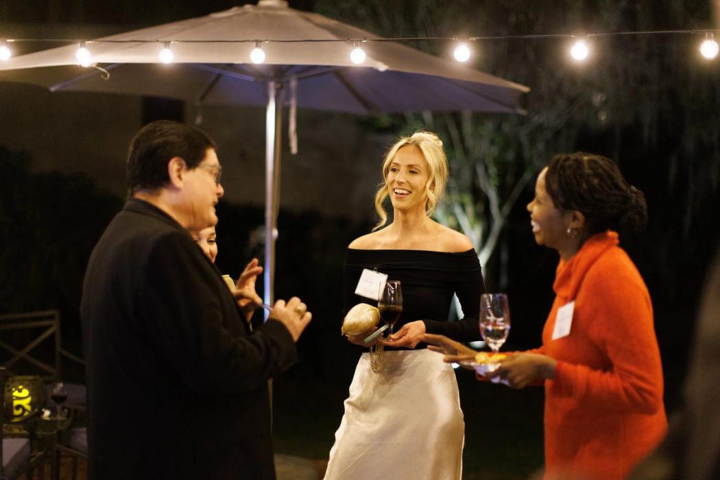 Three alumni outdoors during evening gathering underneath twinkle lights.