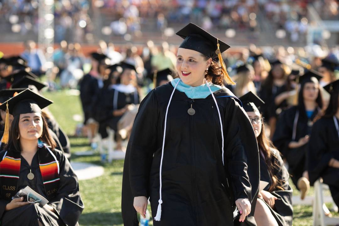 An adult college student walks to receive her degree during a commencement ceremony.