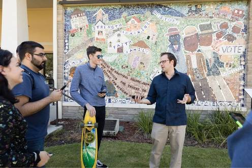 Dan Myers standing in front of a wall mural talking to students.