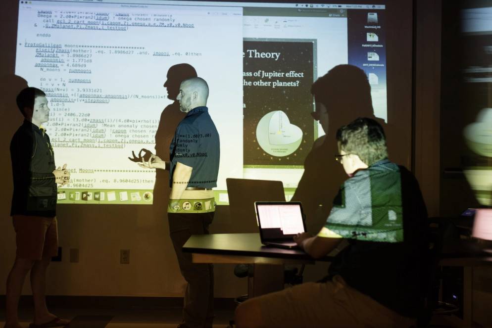 Physics professor Dr. Fuse gives a lecture on astrophysics in a darkened room.