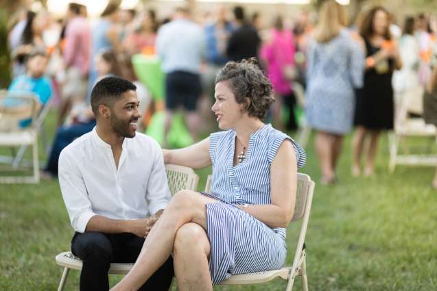 Two students sitting and talking to each other at an outdoor event on the lawn.