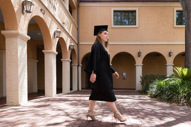 A student in a cap and gown poses on the Rollins College campus.