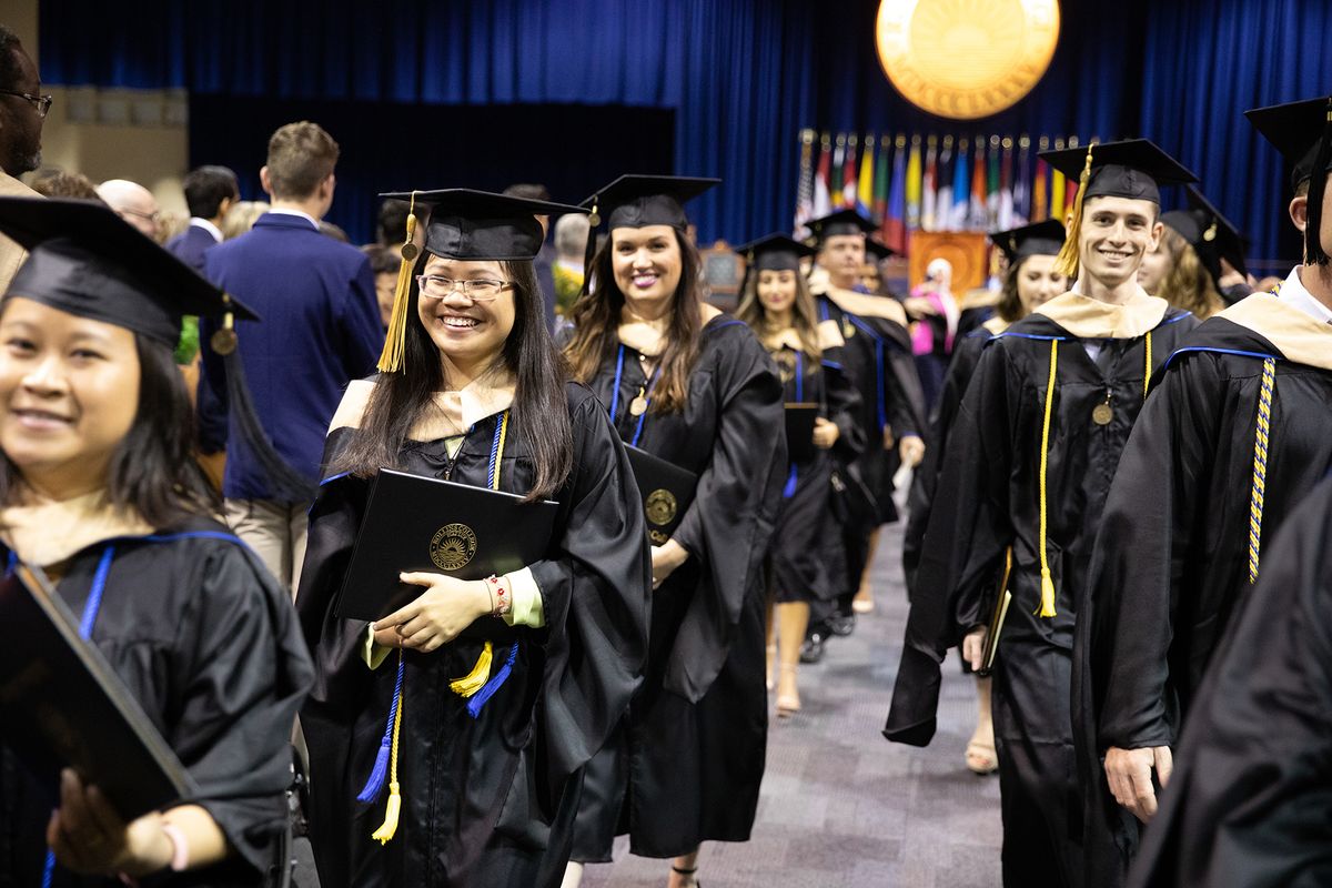 students holding diplomas, walk out of Rollins Commencement ceremony, with smiles on their faces