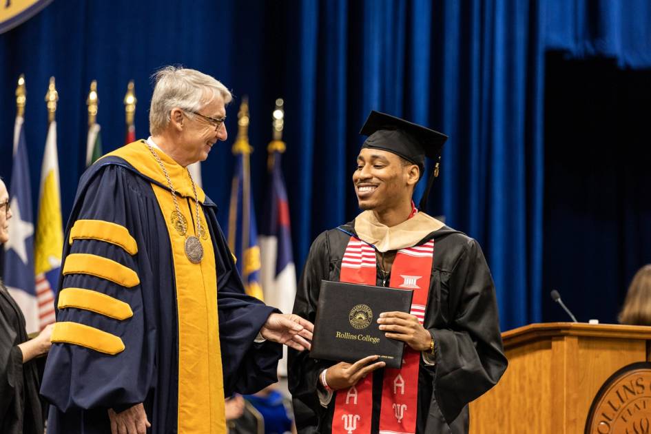 President of Rollins presenting graduation certificate to young graduate with cap and gown